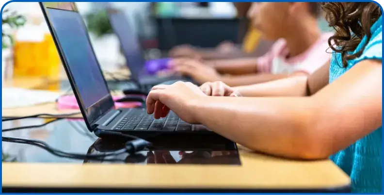 Close-up of hands typing on a laptop keyboard in a classroom
